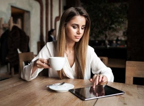 woman drinking coffee and looking at tablet